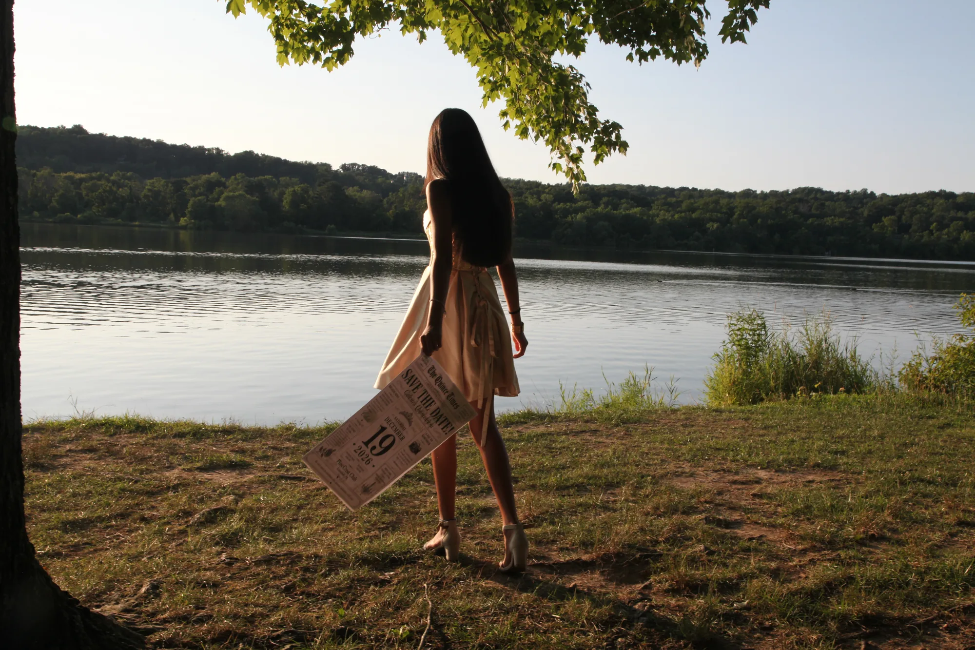 Celeste from behind under a tree, facing the lake at golden hour.